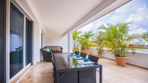Un balcon avec une table en verre, des chaises en osier, un canapé et des plantes en pot.