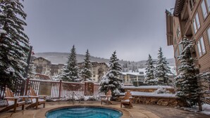 A snow-covered outdoor pool area with lounge chairs, a stone patio, and snow-laden trees.