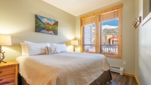 A bedroom with a large bed, two bedside lamps, a painting on the wall, and a window with a view of a building and trees.