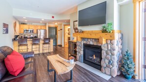 A modern living room with a fireplace, a kitchen area, and a dining space.
