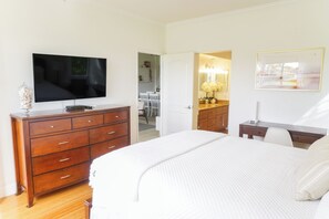 A bedroom with a large bed, a wooden dresser, a television, and a bathroom visible through an open door. - Maui Family Owned & Managed - Wailea Grand Champions Villa (Kihei)