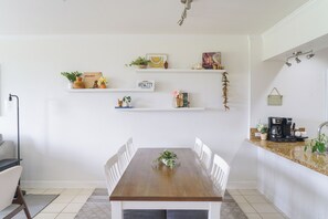 A dining area with a wooden table and white chairs, surrounded by white walls with shelves holding various decorative items and plants. - Maui Family Owned & Managed - Wailea Grand Champions Villa (Kihei)