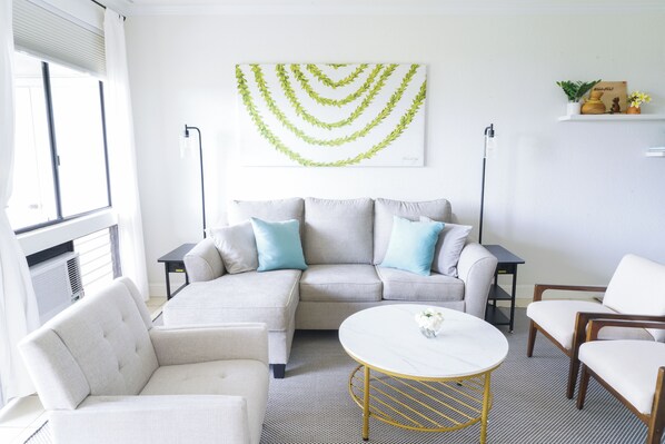 A modern living room with a sectional sofa, a round coffee table, and a decorative wall piece. - Maui Family Owned & Managed - Wailea Grand Champions Villa (Kihei)