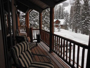 Une terrasse en bois avec un canapé et une rambarde, donnant sur un paysage enneigé parsemé d’arbres et sur une cabane.