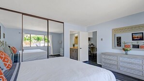 Un dormitorio con una cama grande, un aparador, un espejo y vistas al exterior.