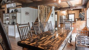 Un interior rústico con una mesa de comedor de madera, sillas y una escalera con vigas a la vista.