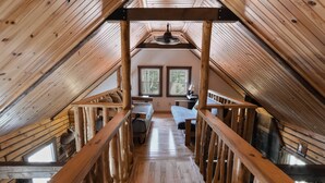 Interior de madera con techo inclinado, una escalera central y una zona de estar con una mesa y sillas.