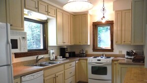 A compact kitchen with a dishwasher, stove, and microwave. There are wooden cabinets and a window providing natural light. - Comfortable & Spacious Ski-In/Ski-Out Cabin (Whitefish)