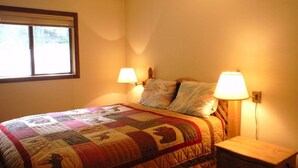 A bedroom with a bed, two bedside lamps, a nightstand, and a window. - Comfortable & Spacious Ski-In/Ski-Out Cabin (Whitefish)