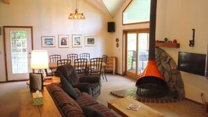 A cozy living room with a fireplace, a dining area with chairs and a table, and a television mounted on the wall. - Comfortable & Spacious Ski-In/Ski-Out Cabin (Whitefish)