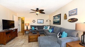 A living room with a grey sofa, wooden coffee table, TV, and ceiling fan. - 315E Lower: Spacious, Remodeled, Ground Level Duplex, Quiet Street, WIFI - 315 E (Avalon)