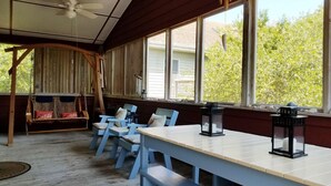 A room with a wooden ceiling, a ceiling fan, a swing, a table with chairs, and large windows with a view of greenery outside. - Hangin' Loose:  Pet friendly, deck, screened porch, ramp (Ocracoke)