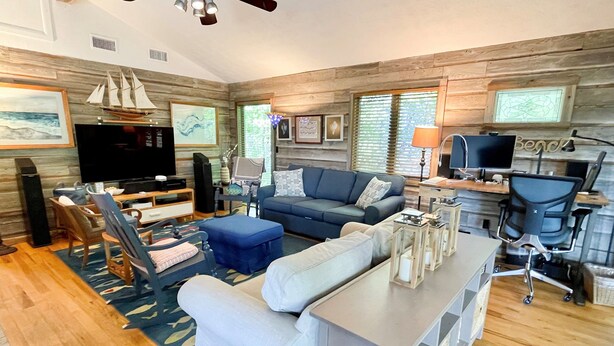 A modern living room with a large TV, a sofa, a coffee table, and a desk with a computer. - Hangin' Loose:  Pet friendly, deck, screened porch, ramp (Ocracoke)