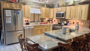 A kitchen with wooden cabinets, a stainless steel refrigerator, a microwave, a stove, and a large island with bar stools. - Hangin' Loose:  Pet friendly, deck, screened porch, ramp (Ocracoke)