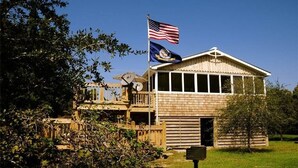 A wooden building with a flagpole, a satellite dish, and a mailbox. - Hangin' Loose:  Pet friendly, deck, screened porch, ramp (Ocracoke)