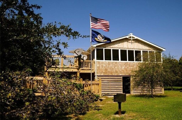 Un bâtiment en bois, orné d’un mât pour drapeau, d’une antenne parabolique et d’une boîte aux lettres.