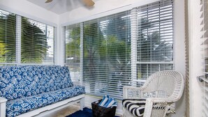 A sunroom with a white bench, a wicker chair, and a blue rug. - Royal Palm Unit 4 4 1,000 sq ft of FUN (Clearwater Beach)