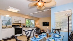 A modern kitchen with white cabinets, a microwave, and a stove. There is a dining area with a glass table set for six, surrounded by chairs. - Royal Palm Unit 4 4 1,000 sq ft of FUN (Clearwater Beach)