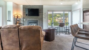 A modern living room with a fireplace, leather sofas, a TV, and a balcony with a view of houses. - Studio that sleeps 4 w/stunning mountain views, hot tub, free wifi, & parking (Copper Mountain)