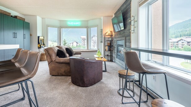 A modern living room with a sofa, chairs, a fireplace, and a large window offering a view of the mountains. - Studio that sleeps 4 w/stunning mountain views, hot tub, free wifi, & parking (Copper Mountain)