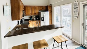 Une cuisine avec des meubles de rangement en bois, un plan de travail en granit, un réfrigérateur et un coin repas équipé de tabourets.