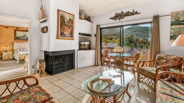 A spacious living room with a fireplace, a dining area with wicker furniture, and a balcony with a scenic view. - A23 - Bahia Vista Condo: 2 Bedroom, 1.75 Bath, Pool (Avalon)