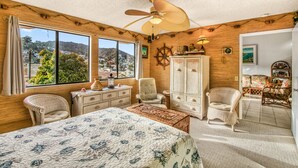 A cozy bedroom with a large bed, two chairs, a dresser, and a view of a town through large windows. - A23 - Bahia Vista Condo: 2 Bedroom, 1.75 Bath, Pool (Avalon)