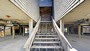 Una escalera de madera conduce a una puerta adornada con una corona, rodeada de paredes sin terminar y materiales de construcción.