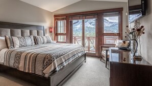 Ein Schlafzimmer mit einem großen Bett, einem Schreibtisch, einem Stuhl und Blick auf Berge durch die Fenster.