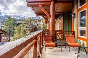 Un balcón de madera con sillas naranjas y una mesa, con vista a una zona montañosa con edificios.