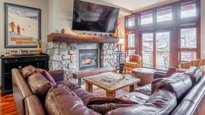 Ein gemütliches Wohnzimmer mit Kamin aus Stein, Ledersofas, einem Holztisch und einem großen Fernseher, der über dem Kamin angebracht ist.