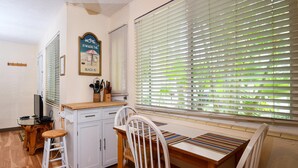 Een kleine keuken met witte kastjes, een houten aanrecht en een eettafel met witte stoelen.