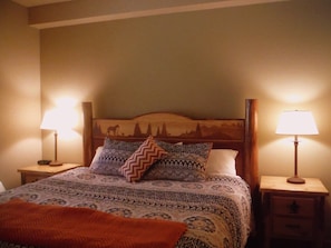 A bed with patterned bedding, two bedside lamps, and a nightstand with a drawer.
