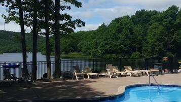 A swimming pool with lounge chairs and a view of a lake and forest.