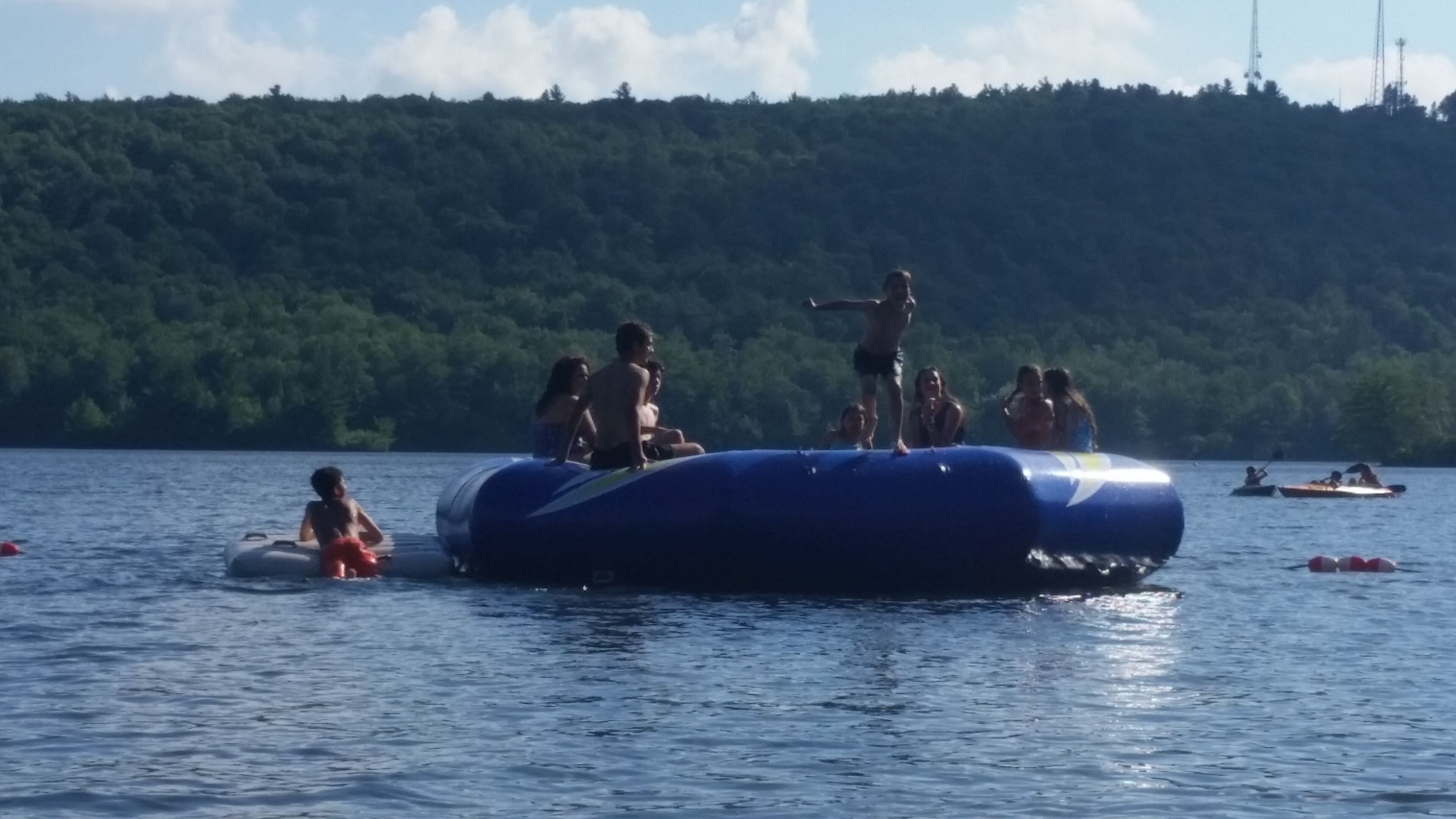 A group of people on a blue raft-like structure in a body of water, surrounded by a forested area.