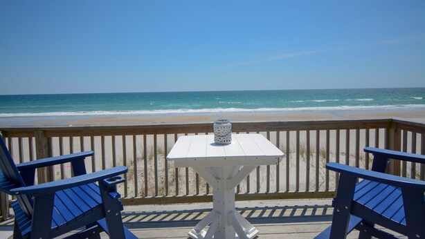 A deck with two blue chairs and a white table, overlooking a beach with the ocean. - Oceanfront 3BR townhome in Surf City with stunning views at Turtle Cove 908D. (Surf City)