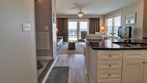 A modern kitchen with a black countertop and white cabinetry, a dining area with a table and chairs, and a view of the ocean through large windows. - Oceanfront 3BR townhome in Surf City with stunning views at Turtle Cove 908D. (Surf City)