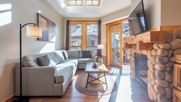 A cozy living room with a sofa, a coffee table, and a fireplace. There are large windows and a skylight.