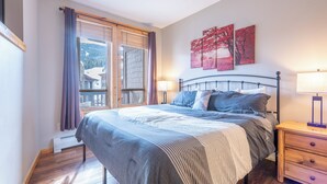A bedroom with a bed, nightstands, a window with curtains, and artwork on the wall.