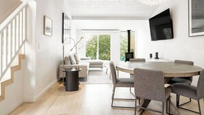 Ein modernes Wohnzimmer mit einem runden Holztisch, grauen Sofas und einer Treppe links.
