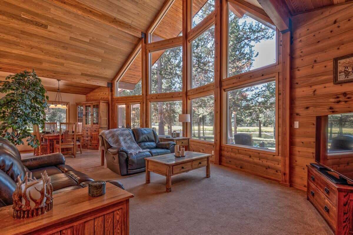 A spacious living room with a high ceiling, large windows, and wooden walls.