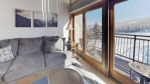 A modern living room with a grey sofa, a coffee table, and a view of a snowy landscape through large glass doors.