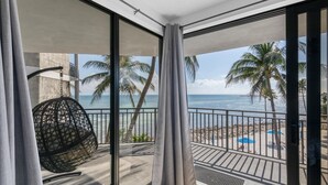 Un balcón con vista a la playa y al océano, un sillón colgante y una barandilla de metal.