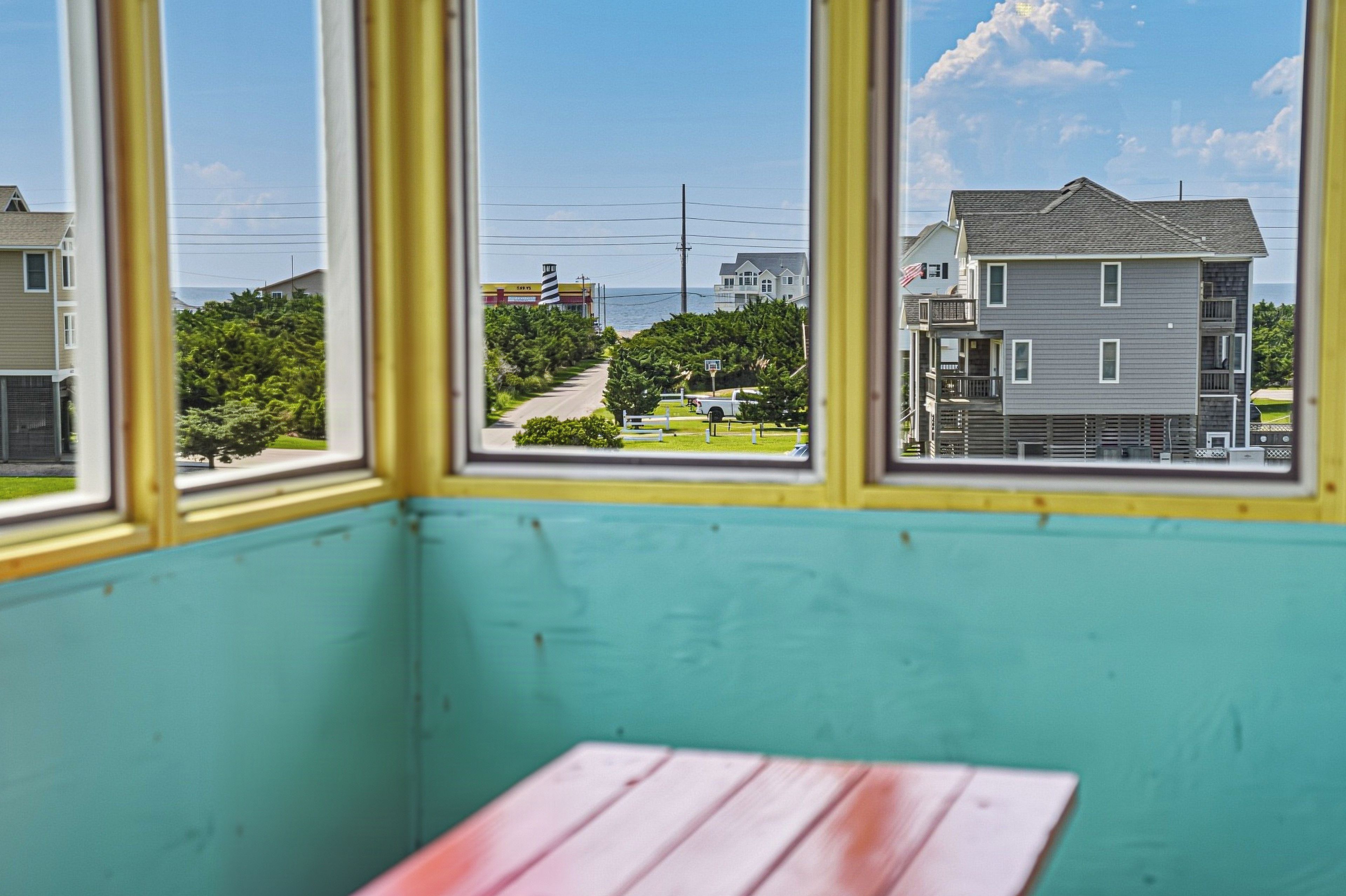 A room with a window overlooking a street, a bench, and a view of a building across the street.