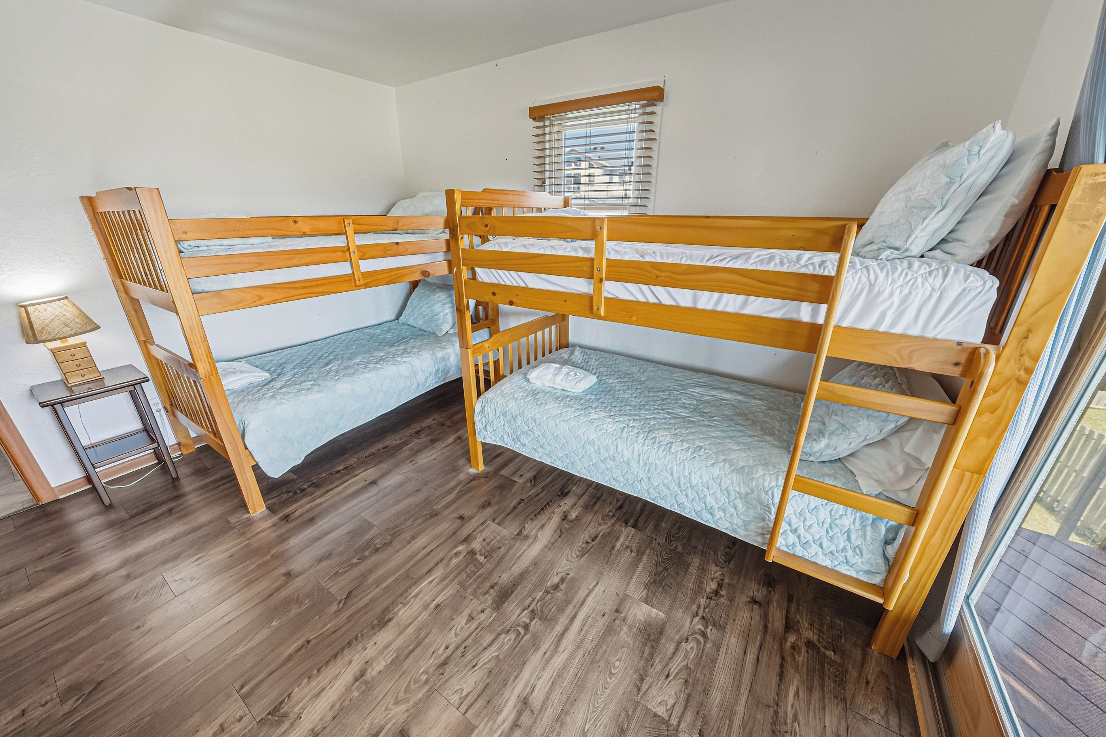 A bunk bed room with wooden frames, a small table, and a window with blinds.