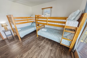 A bunk bed room with wooden frames, a small table, and a window with blinds.