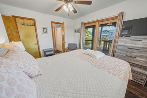 Un dormitorio con cama, escritorio, silla, ventilador de techo y vista al exterior.