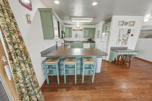 A kitchen with green cabinets, a central island with bar stools, and a wooden floor.