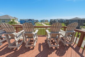 A deck with four Adirondack chairs facing a view of a coastal residential area with multiple buildings.