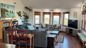 A living room with a sofa, chairs, a coffee table, a bookshelf, a TV, and large windows. -     7BR Coastal Escape ,Ocean and Sound Views, Pool, Hot Tub & Pet Friendly (Rodanthe)